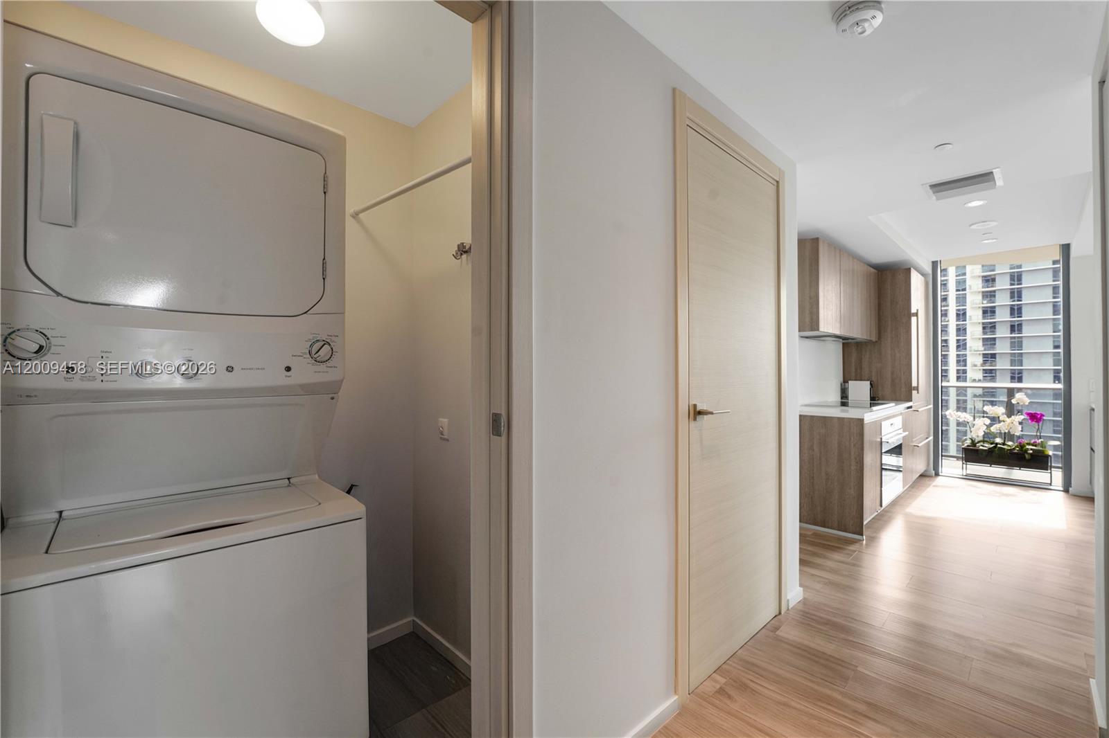 A stacked washer and dryer sit next to a doorway leading to a modern kitchen — 801 S Miami Ave # 3109, Miami FL 33130, MIAMI, FL