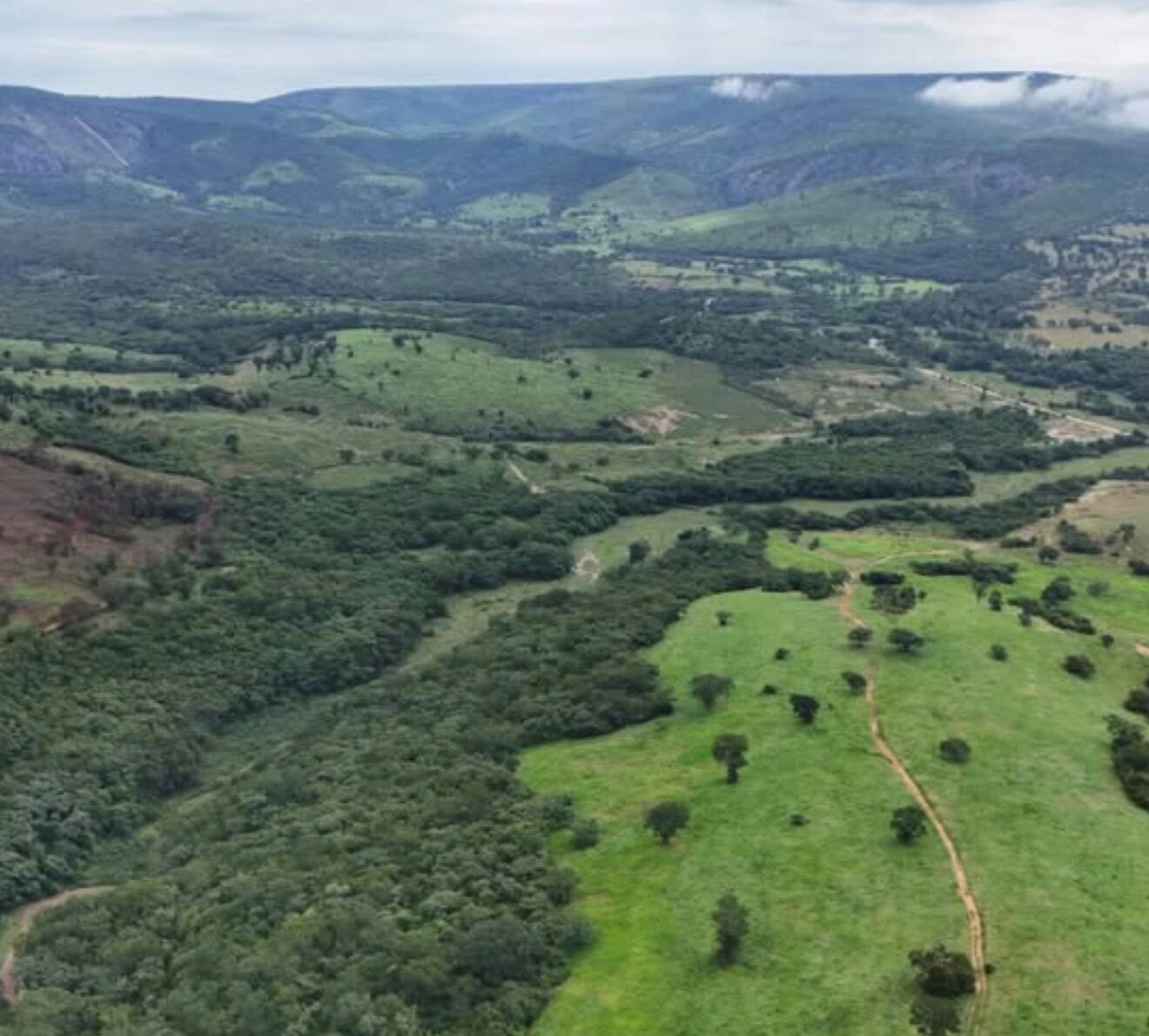 An aerial view shows a landscape with patches of forest, grassy fields, and distant mountains — 01 Estrada Itinga, FL