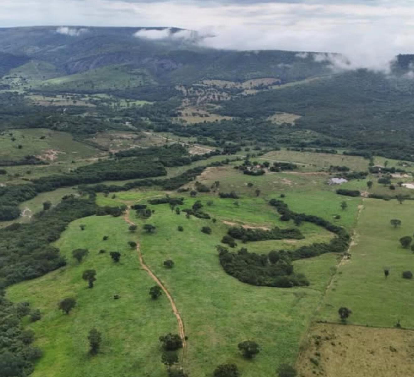An aerial view of a green, hilly landscape with pastures, scattered trees, and dirt paths — 01 Estrada Itinga, FL