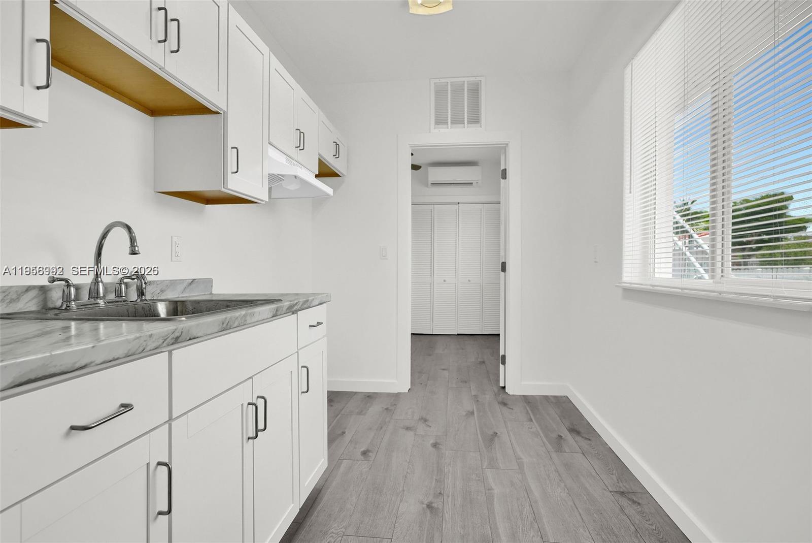 A kitchen features white cabinets, a marble-patterned countertop, and gray wood-look flooring — 600 NW 25th Ct, Miami FL 33125, MIAMI, FL