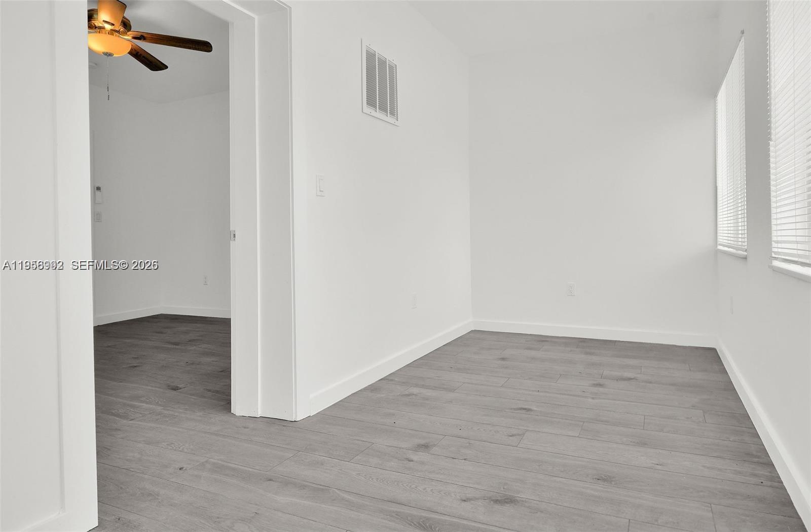 An empty room with white walls, gray wood-look flooring, and a doorway to another room — 600 NW 25th Ct, Miami FL 33125, MIAMI, FL
