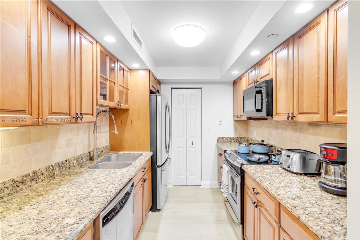 A galley kitchen features light wood cabinets, granite countertops, and stainless steel appliances — 3000 N Ocean Dr # 3B, Singer Island FL 33404, SINGER ISLAND, FL
