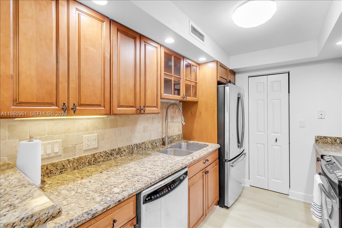A kitchen features wood cabinets, granite countertops, a stainless steel refrigerator, and a double sink — 3000 N Ocean Dr # 3B, Singer Island FL 33404, SINGER ISLAND, FL