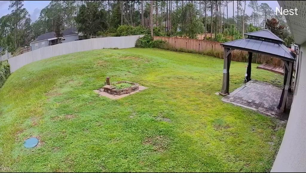 A backyard features a grassy lawn, a stone fire pit, and a covered gazebo — 1730 EAST PARKWAY, DELAND, FL