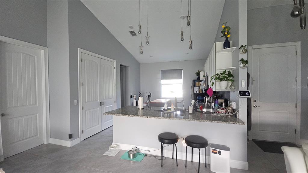 A kitchen with a granite island, bar stools, and grey walls under a vaulted ceiling — 1730 EAST PARKWAY, DELAND, FL
