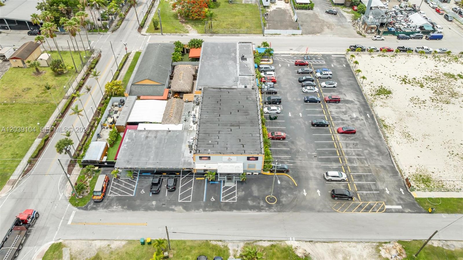 An aerial view shows a commercial building with a large parking lot and outdoor seating — HOMESTEAD, FL