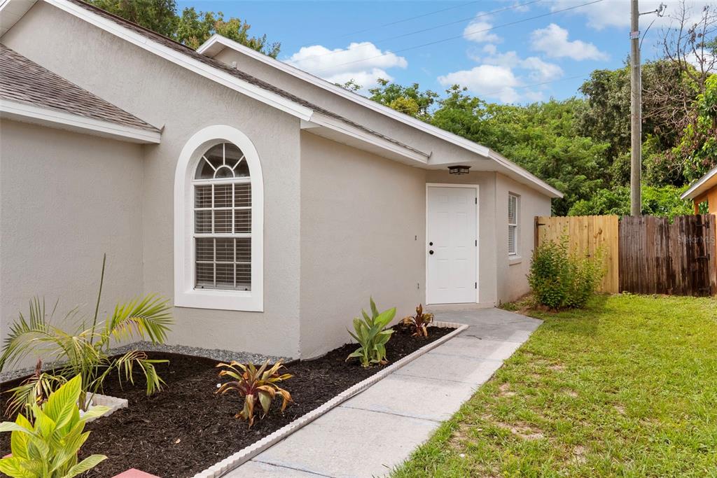 A beige house exterior features a white arched window, a side door, and landscaping — 5459 SEEDLING LANE, ORLANDO, FL