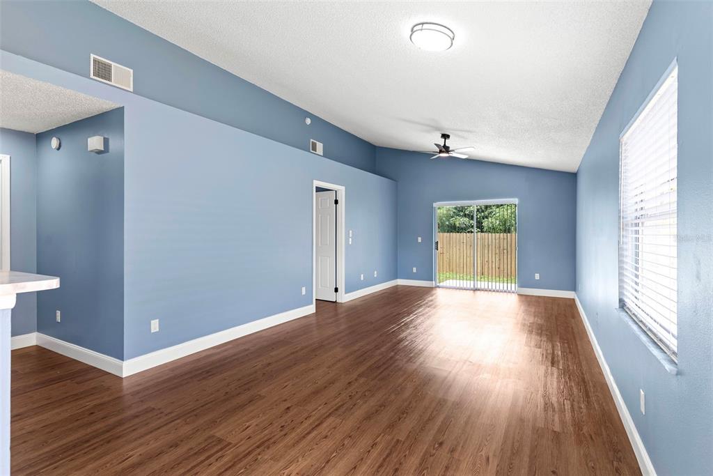 An empty living room features blue walls, wood-look flooring, a vaulted ceiling, and sliding glass doors — 5459 SEEDLING LANE, ORLANDO, FL