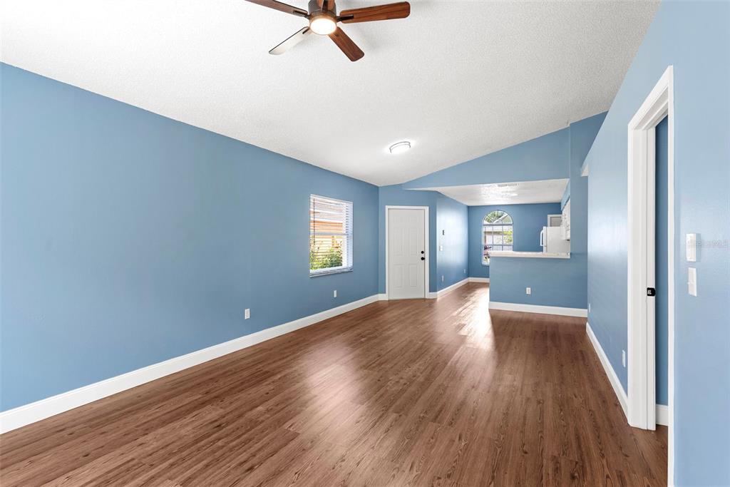 An empty room with blue walls, wood-look flooring, a ceiling fan, and an adjacent kitchen — 5459 SEEDLING LANE, ORLANDO, FL