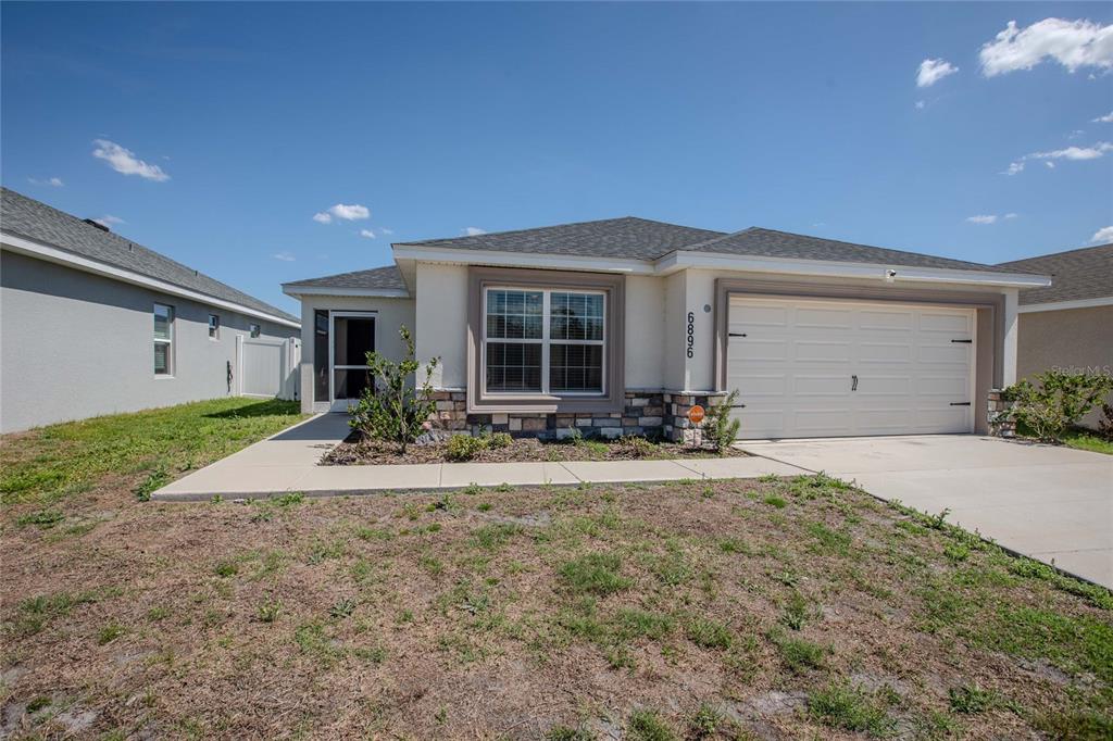 A single-story house features a beige stucco exterior, stone accents, and a two-car garage — 6896 PEBBLEBROOKE WAY, ZEPHYRHILLS, FL