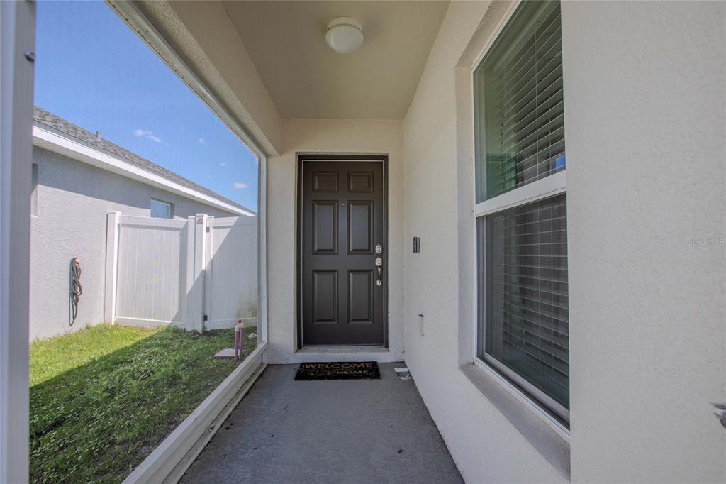 A covered entryway features a dark front door, a concrete floor, and a side window — 6896 PEBBLEBROOKE WAY, ZEPHYRHILLS, FL