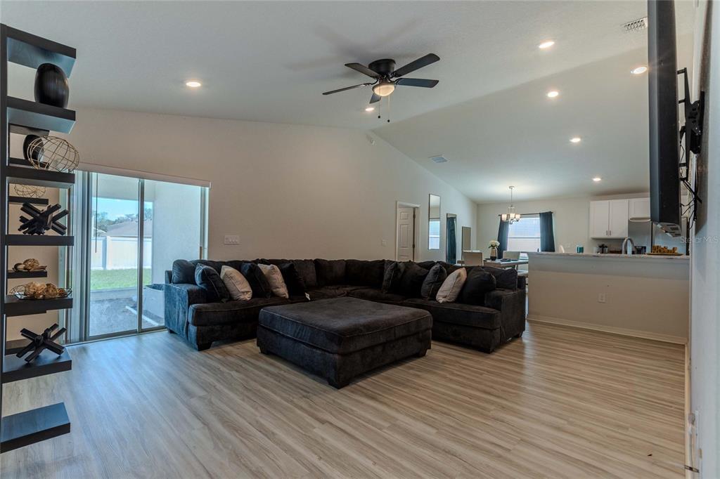 A living room with a large sectional sofa, vaulted ceilings, and light wood-look flooring — 6896 PEBBLEBROOKE WAY, ZEPHYRHILLS, FL
