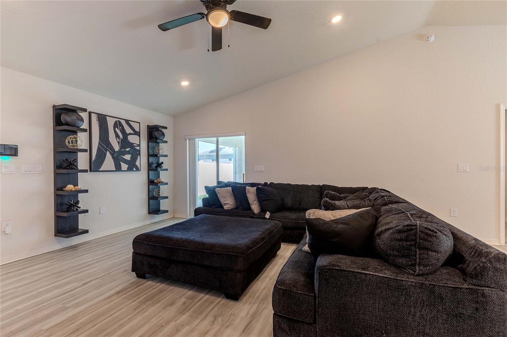 A living room features a large dark sectional sofa, a matching ottoman, and wall-mounted shelving — 6896 PEBBLEBROOKE WAY, ZEPHYRHILLS, FL
