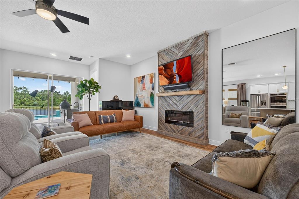 A living room features a chevron-patterned wood fireplace, a leather sofa, and a large mirror — 4282 AMPED WAY, LAND O LAKES, FL