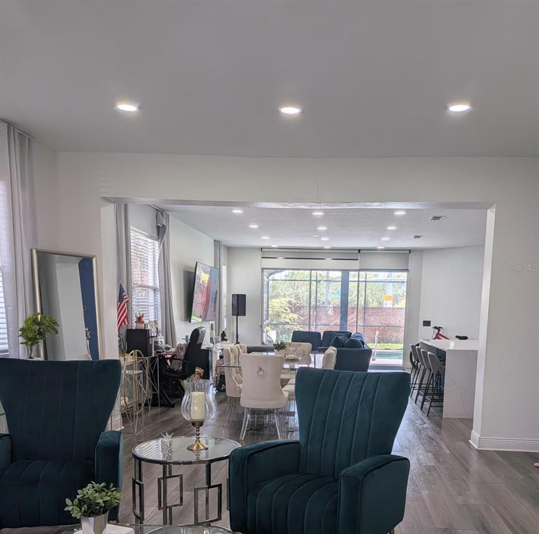 An open-concept living and dining area features teal armchairs, a dining set, and kitchen island — 2047 BEARING LANE, KISSIMMEE, FL