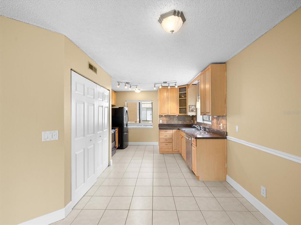 A kitchen features light wood cabinets, dark countertops, tile flooring, and a white closet door — 1550 S BELCHER ROAD UNIT 421, CLEARWATER, FL