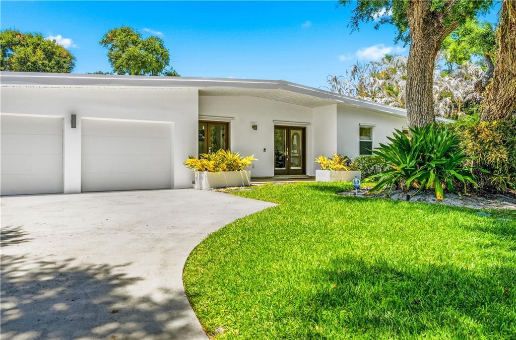 A white single-story house with a two-car garage, front lawn, and mature trees — VERO BEACH, FL