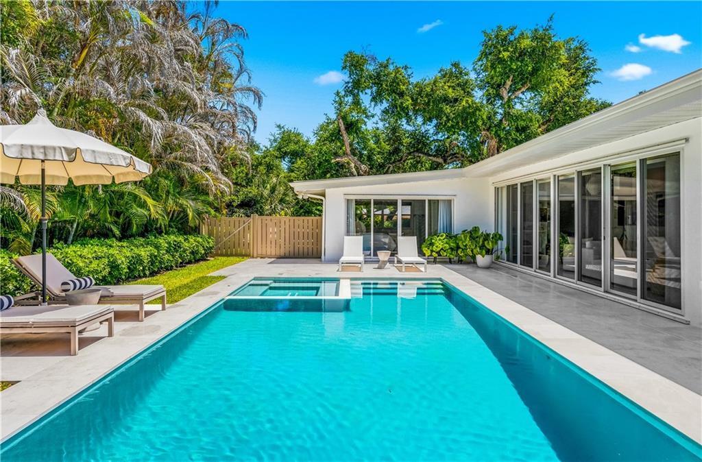 A rectangular swimming pool with an integrated spa sits beside a white house with sliding doors — VERO BEACH, FL