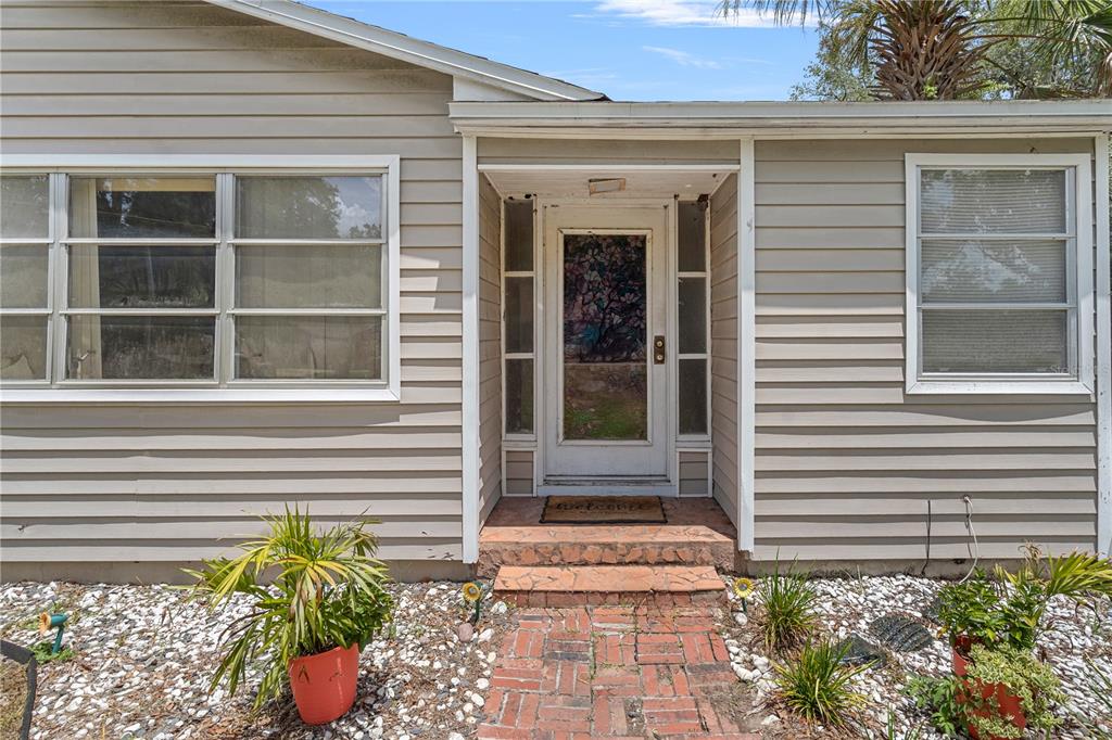 The exterior of a house features beige horizontal siding, a brick walkway, and a front door — 26015 SACKAMAXON DRIVE, SORRENTO, FL