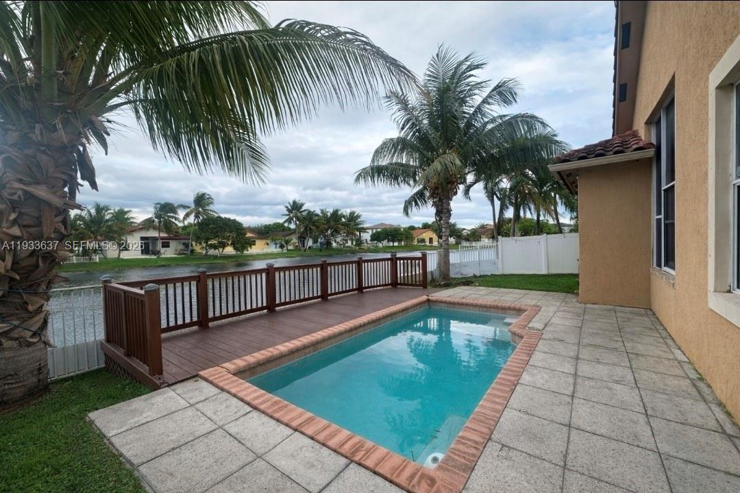 A backyard features a rectangular swimming pool, a wooden deck, and a view of a lake — 13877 SW 50th St, Miramar FL 33027, MIRAMAR, FL