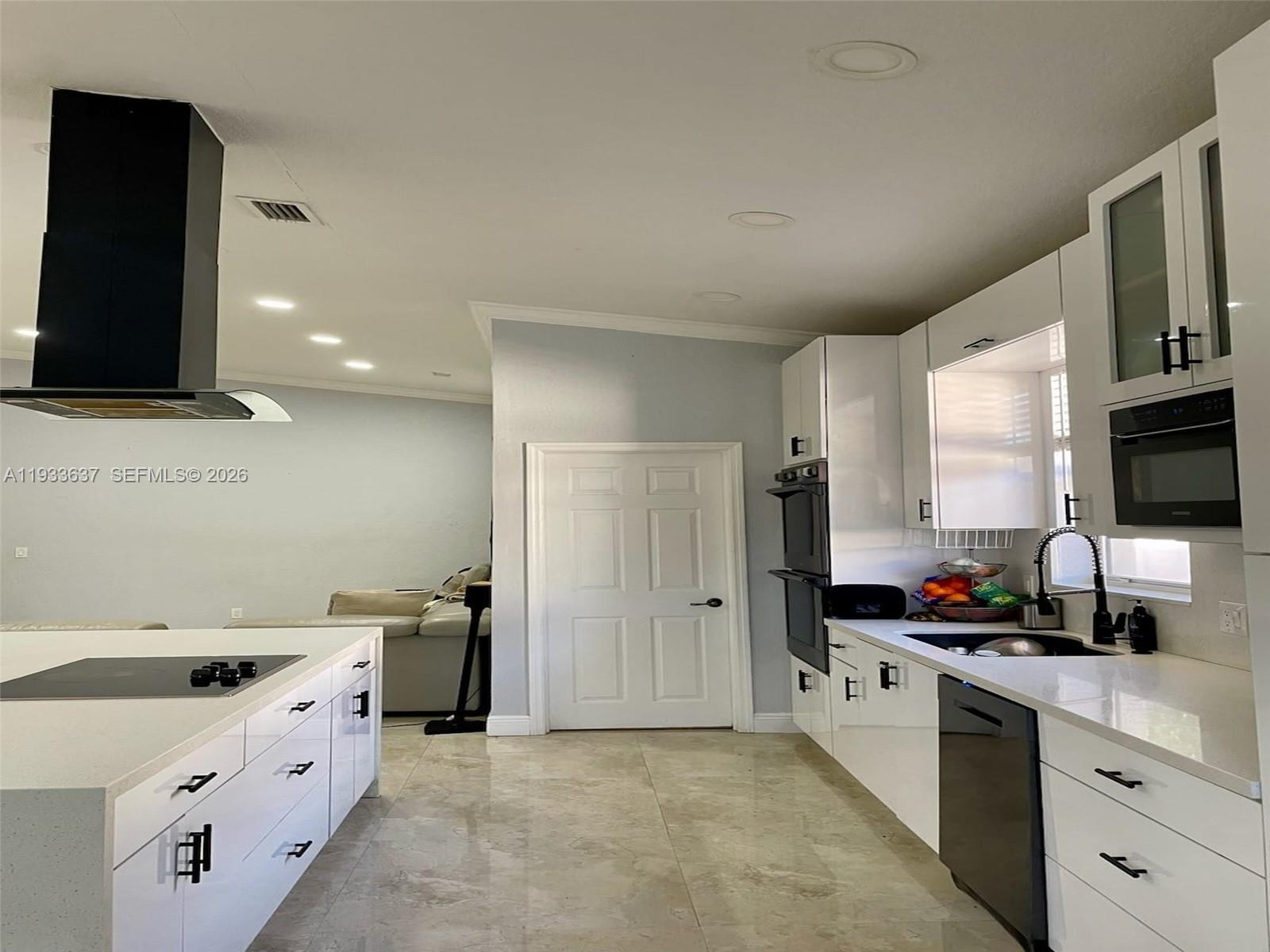 A modern kitchen features white cabinetry, a central island with a cooktop, and tile flooring — 13877 SW 50th St, Miramar FL 33027, MIRAMAR, FL