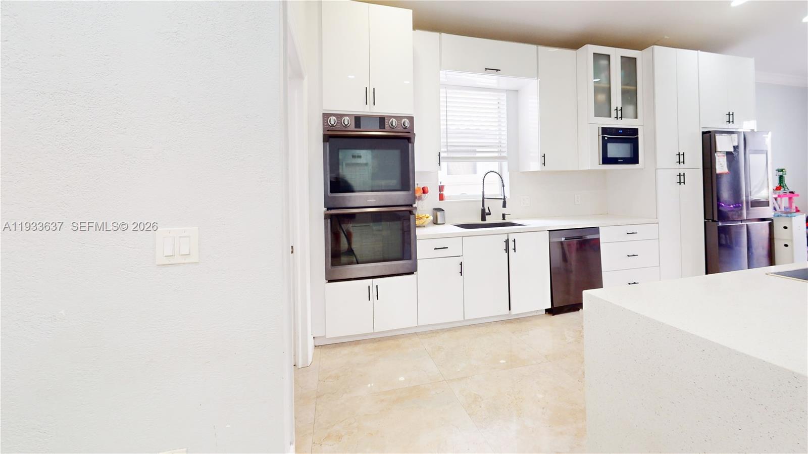 A modern kitchen features white cabinetry, stainless steel appliances, and light-colored tile flooring — 13877 SW 50th St, Miramar FL 33027, MIRAMAR, FL