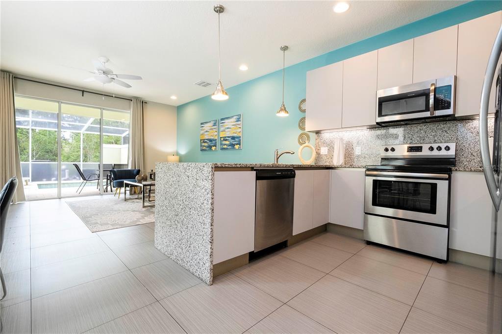 A modern kitchen with white cabinets, granite countertops, and a turquoise accent wall — 1637 TRANQUIL AVENUE, CLERMONT, FL