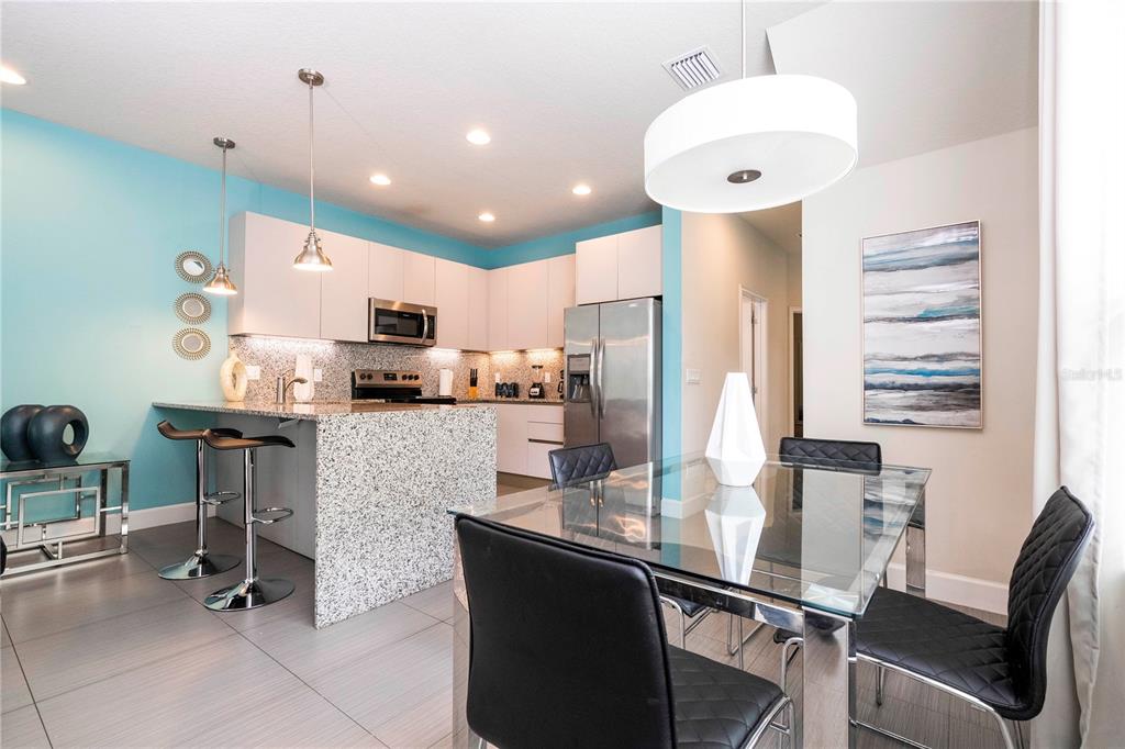 A modern kitchen features white cabinets, granite countertops, a breakfast bar, and an adjacent dining area — 1637 TRANQUIL AVENUE, CLERMONT, FL