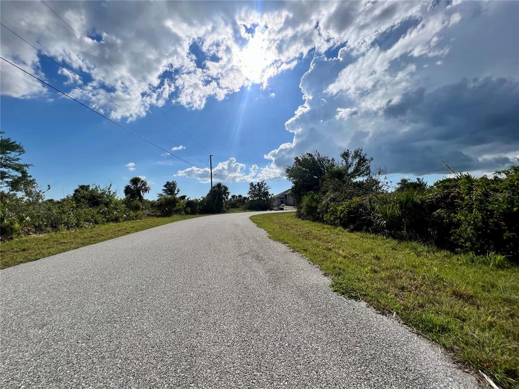 A paved road winds through a sunny, undeveloped landscape with scattered trees and shrubs — 14298 MONTMARTE AVENUE, PORT CHARLOTTE, FL
