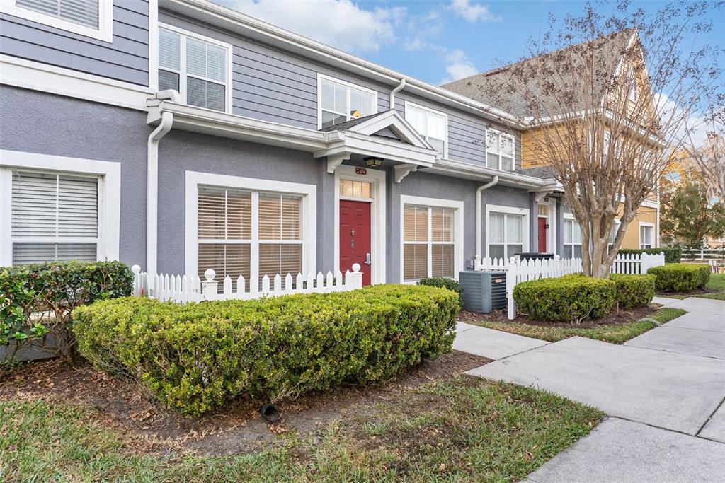 A gray townhouse exterior features a red front door, white trim, and a small hedge — 2608 LODI CIRCLE UNIT 104, KISSIMMEE, FL