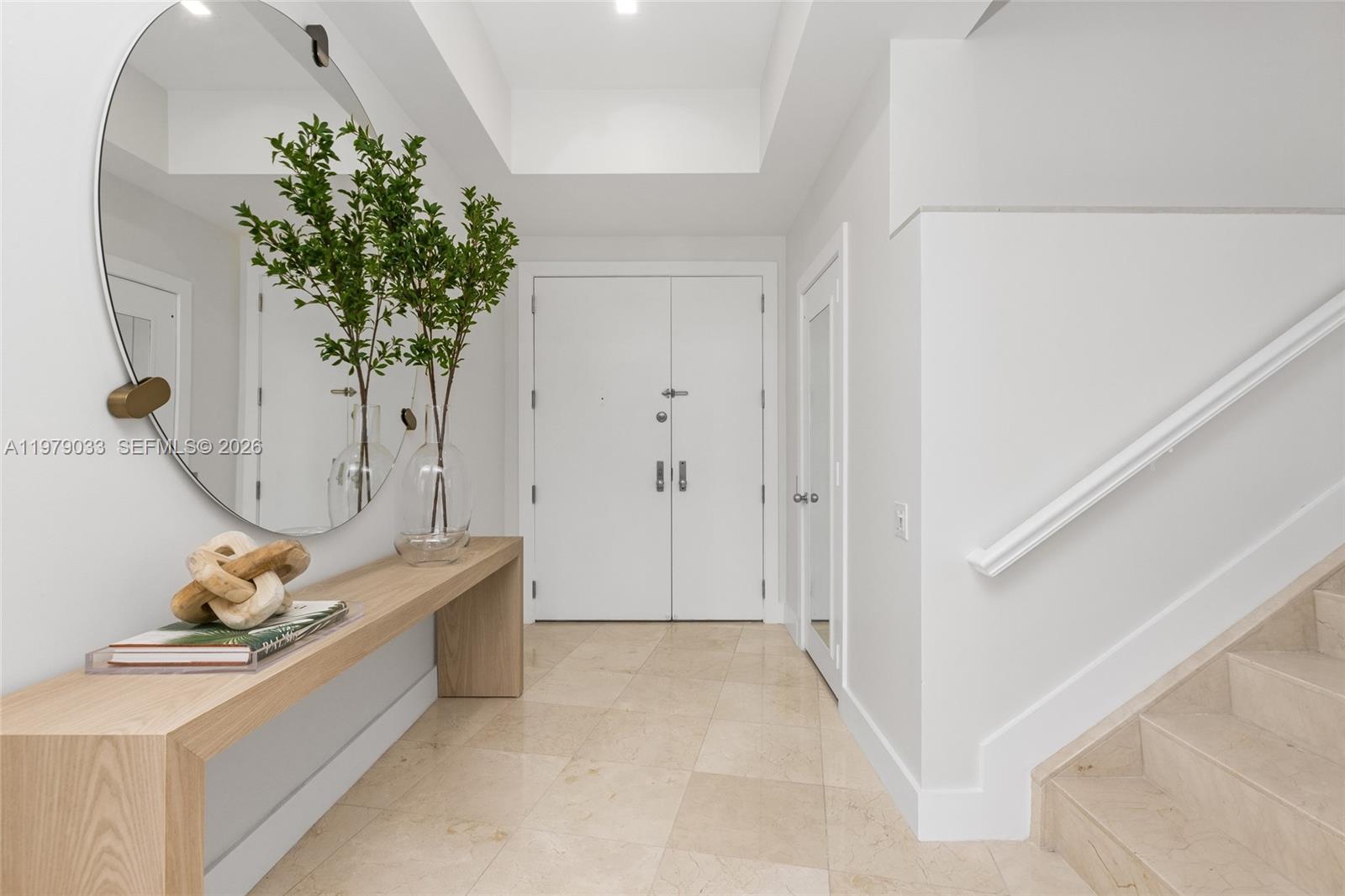 A bright entryway features a light wood console table, a round mirror, and stone flooring — 808 Brickell Key Dr # 3901, Miami FL 33131, MIAMI, FL