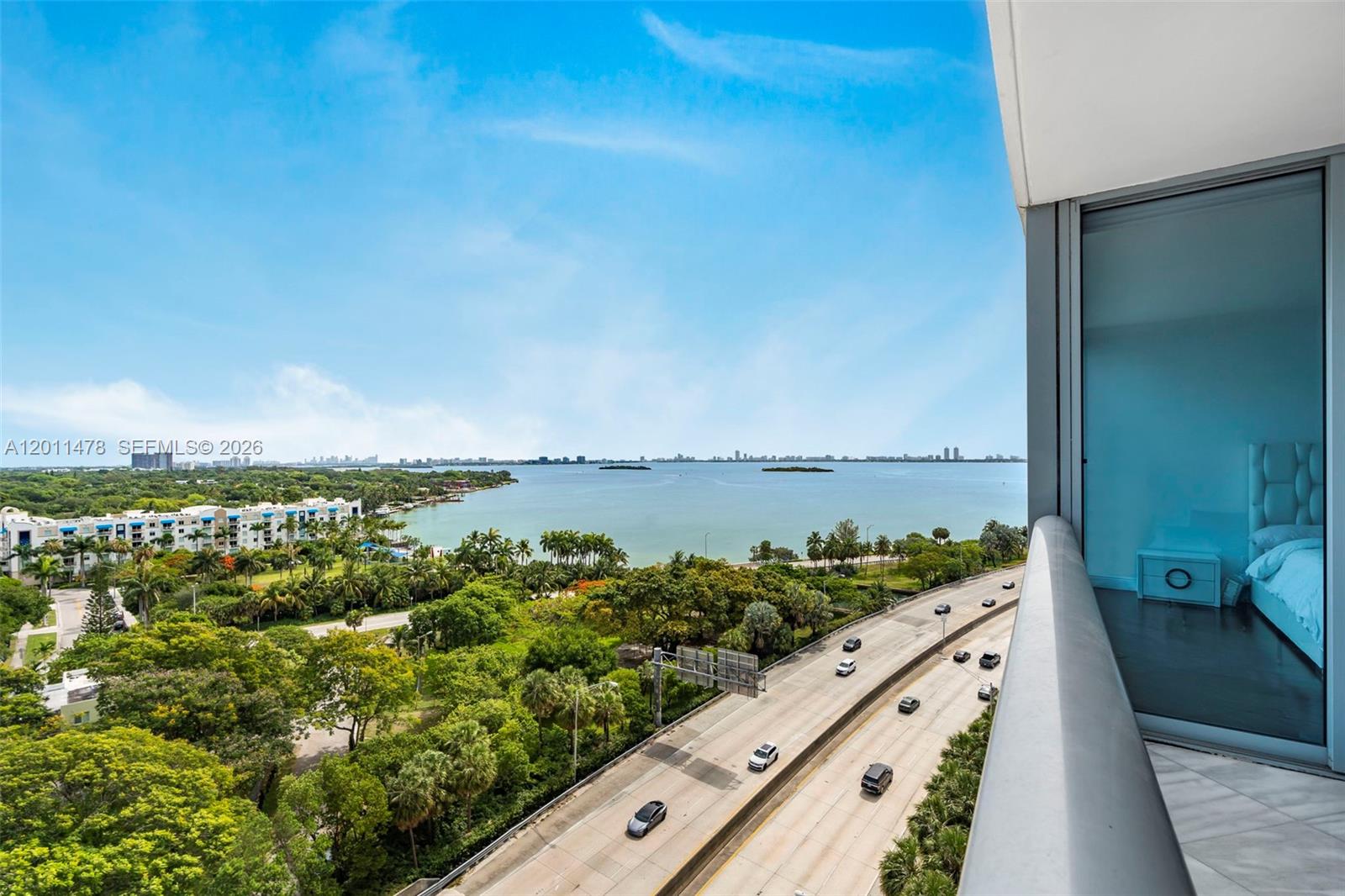 An elevated balcony view overlooks a highway, lush greenery, and a large body of water — 601 NE 36th St # 1103, Miami FL 33137, MIAMI, FL