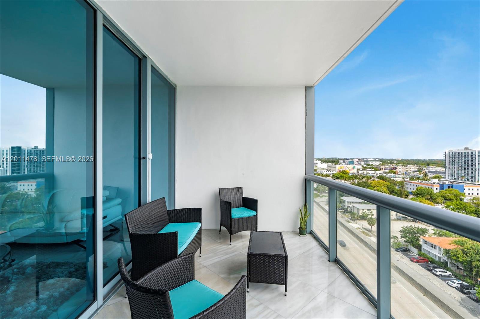 A balcony features wicker furniture with teal cushions and a view of the city — 601 NE 36th St # 1103, Miami FL 33137, MIAMI, FL