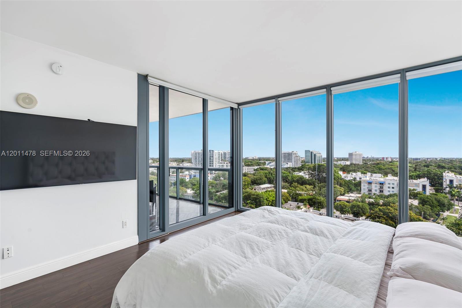 A bedroom features a large bed, dark wood flooring, and floor-to-ceiling windows with city views — 601 NE 36th St # 1103, Miami FL 33137, MIAMI, FL
