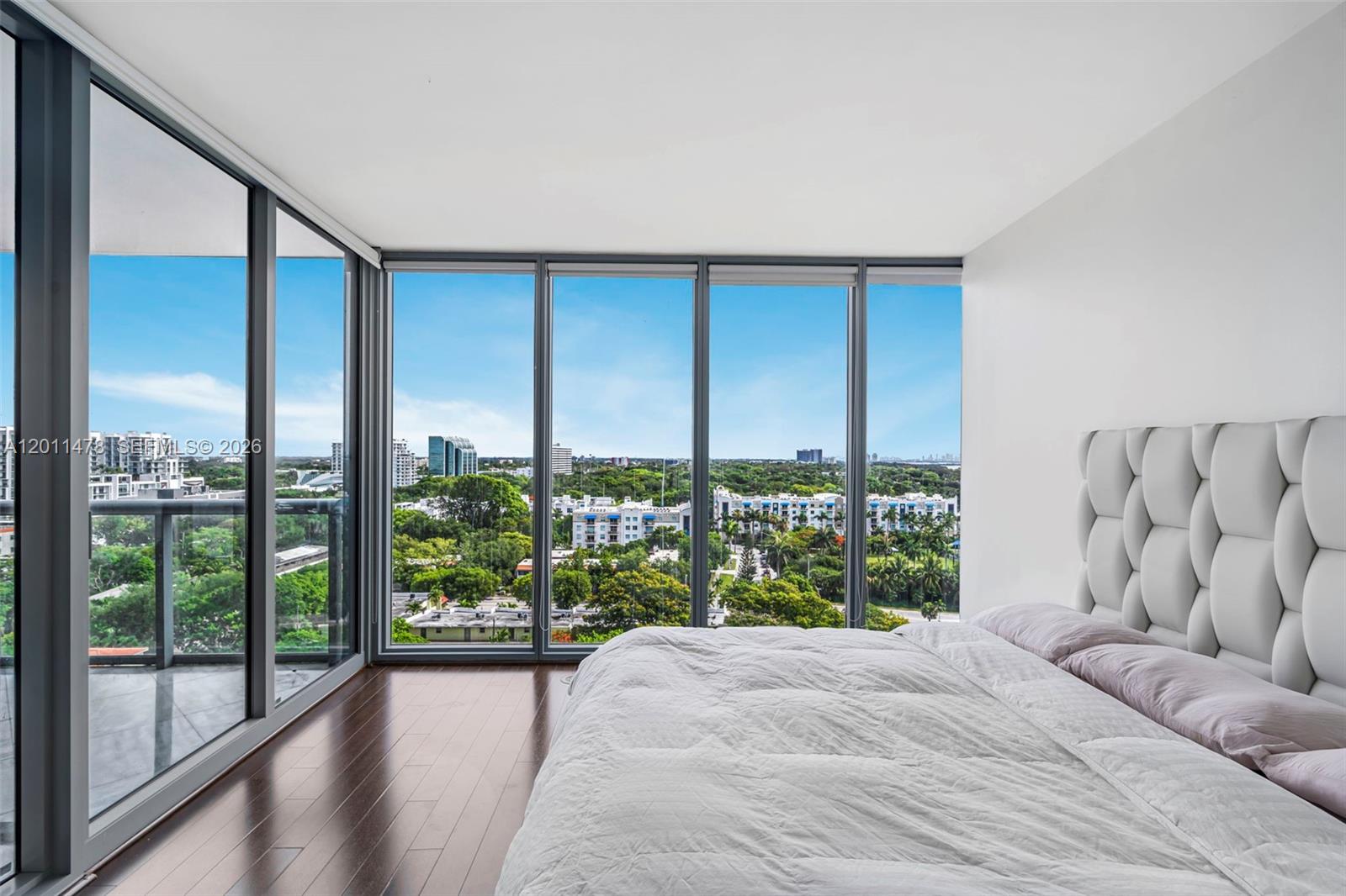 A bedroom features a white tufted headboard, dark wood floors, and floor-to-ceiling windows with views — 601 NE 36th St # 1103, Miami FL 33137, MIAMI, FL