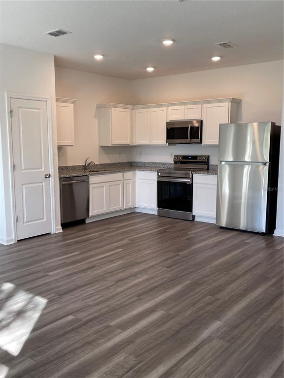 A kitchen with white cabinets, stainless steel appliances, granite countertops, and wood-look flooring — 6157 DAERR RIDGE UNIT 6157, ZEPHYRHILLS, FL
