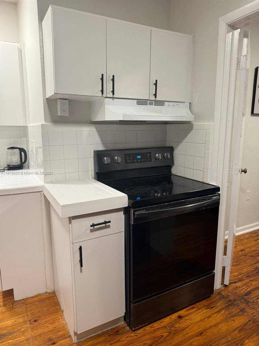 A kitchen features white cabinets, a black electric stove, and a white tiled backsplash — 1289 Marseille Dr # 46, Miami Beach FL 33141, MIAMI BEACH, FL