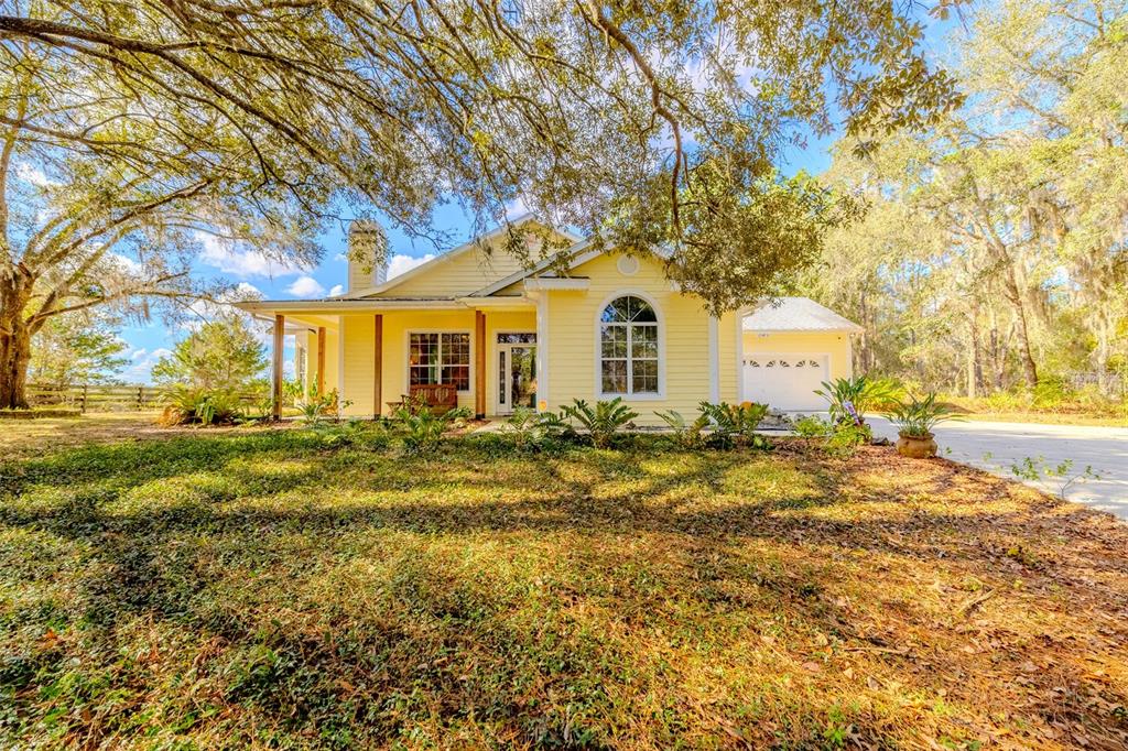 A yellow single-story house with a front porch and a driveway sits under large trees — 12480 S FERN POINT, FLORAL CITY, FL