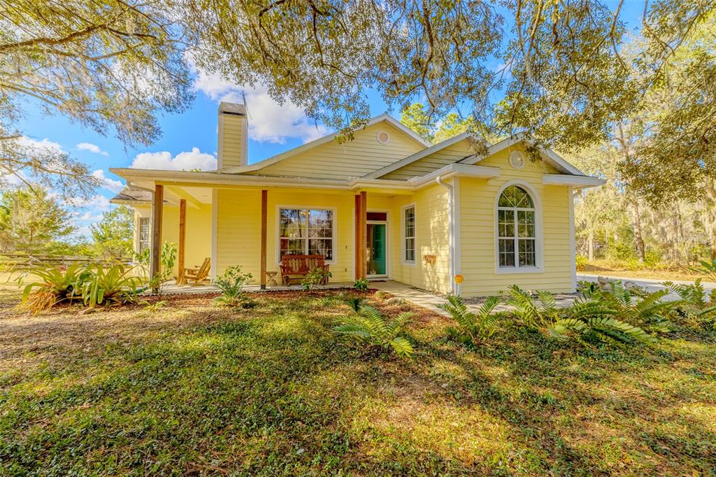 A yellow house with a covered porch, a chimney, and large trees in the yard — 12480 S FERN POINT, FLORAL CITY, FL
