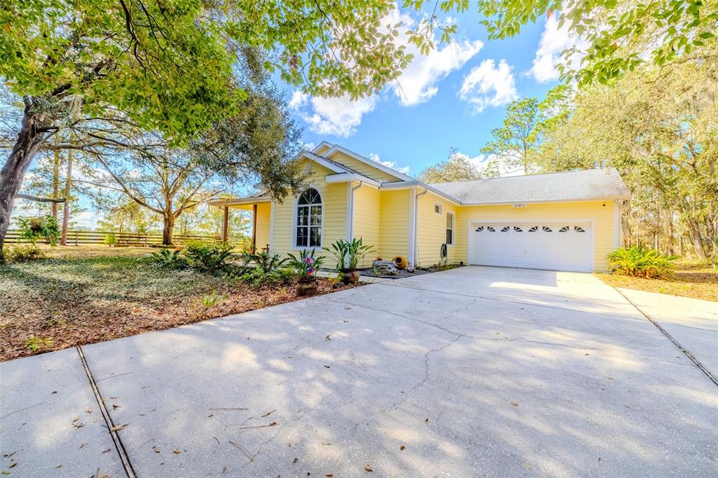 A yellow single-story house with a white garage and a concrete driveway under large trees — 12480 S FERN POINT, FLORAL CITY, FL