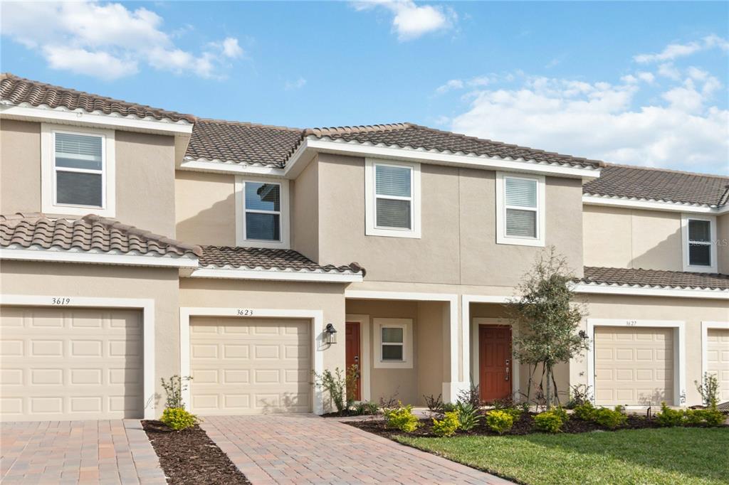A row of two-story townhouses with beige stucco walls, brown tile roofs, and paved driveways — 3623 LANDING NET DRIVE, KISSIMMEE, FL
