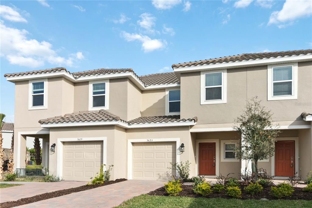 A two-story duplex with beige stucco walls, two garages, and two red front doors — 3623 LANDING NET DRIVE, KISSIMMEE, FL
