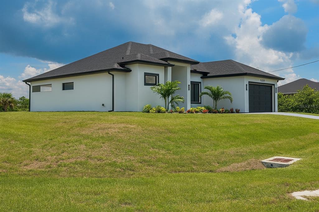A modern, white single-story house with a dark roof and garage sits on a grassy lot — 1321 NE 19 TERRACE, CAPE CORAL, FL