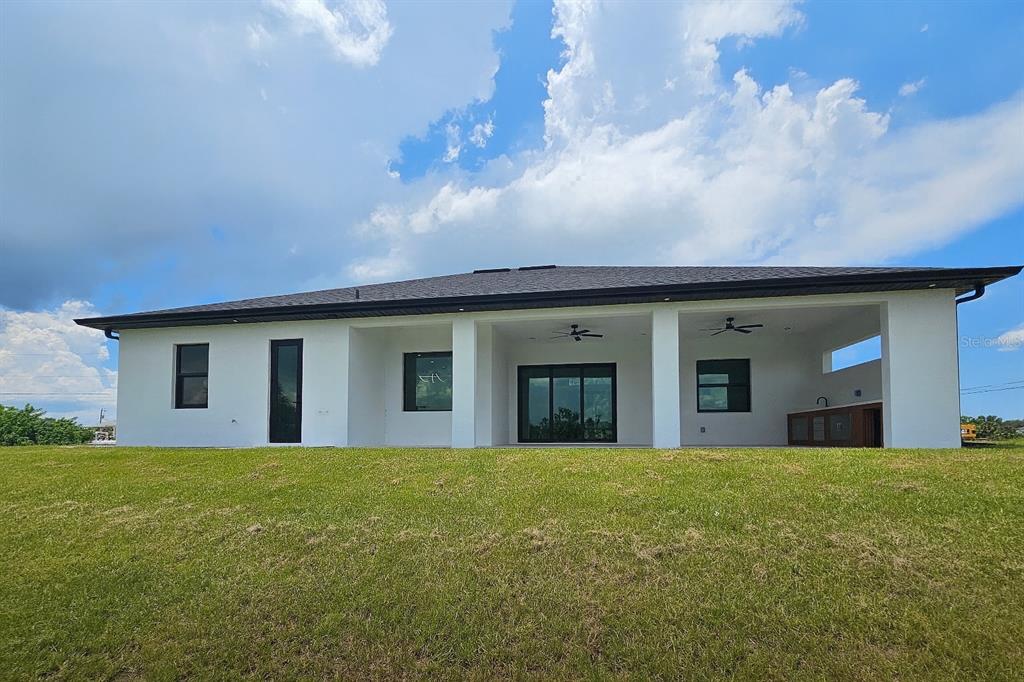 The rear exterior of a modern white house features a covered patio and grassy yard — 1321 NE 19 TERRACE, CAPE CORAL, FL
