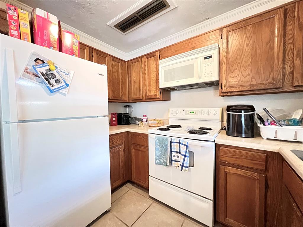 A kitchen features wood cabinets, white appliances, and tile flooring — 2811 SW ARCHER ROAD UNIT 190, GAINESVILLE, FL