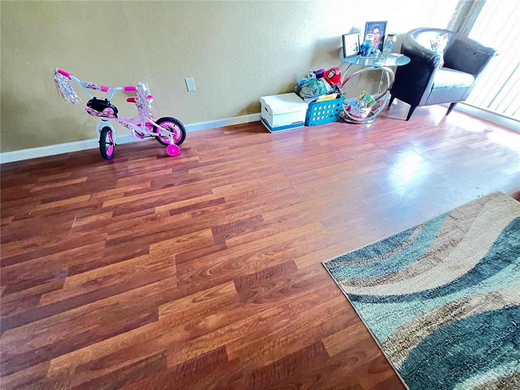A room with wood-look flooring, a pink child's bicycle, a side table, and an armchair — 2811 SW ARCHER ROAD UNIT 190, GAINESVILLE, FL