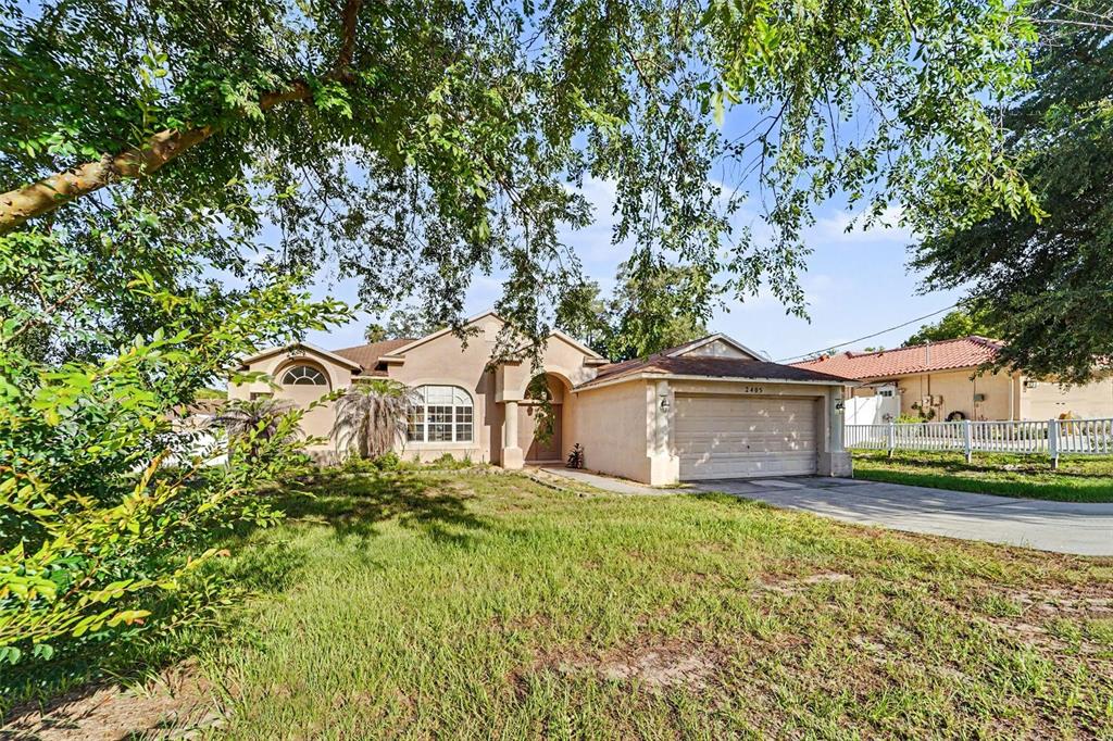 A single-story tan stucco house with a two-car garage and a large front lawn — 2405 AINSWORTH AVENUE, SPRING HILL, FL