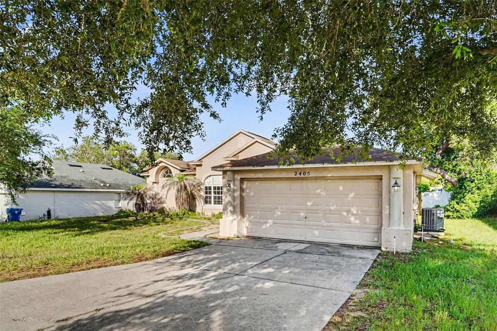 A single-story house with a beige stucco exterior, a two-car garage, and a concrete driveway — 2405 AINSWORTH AVENUE, SPRING HILL, FL