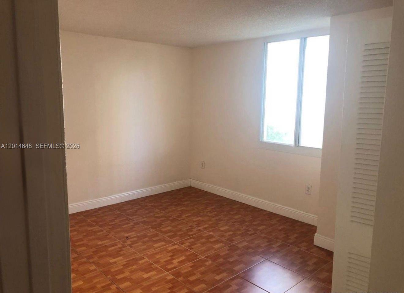 An empty room features light-colored walls, a window, and brown patterned tile flooring — 800 N Miami Ave # 407, Miami FL 33136, MIAMI, FL