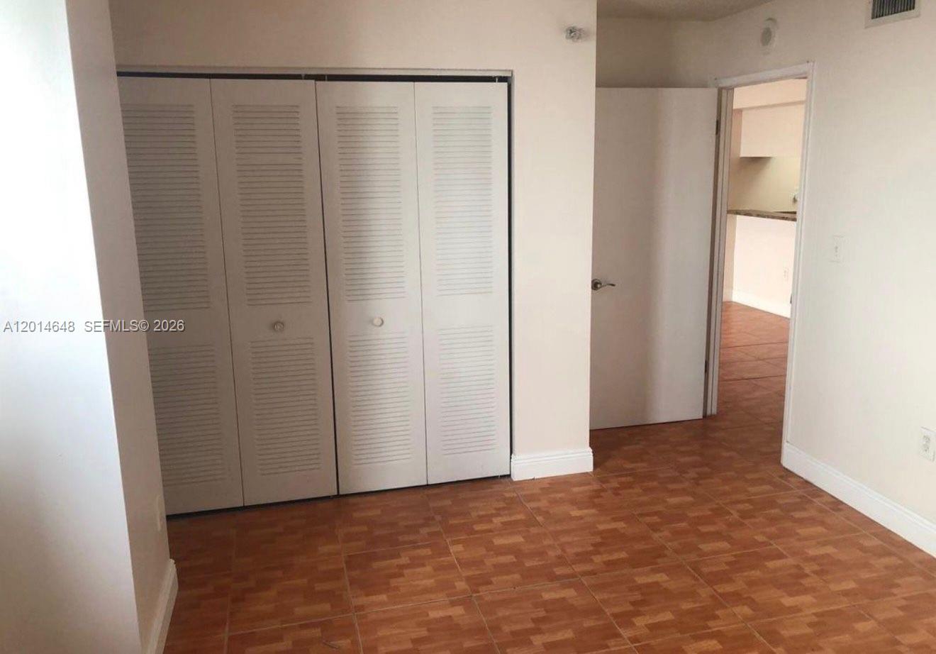 A room with light-colored walls, louvered closet doors, and brown tiled flooring — 800 N Miami Ave # 407, Miami FL 33136, MIAMI, FL